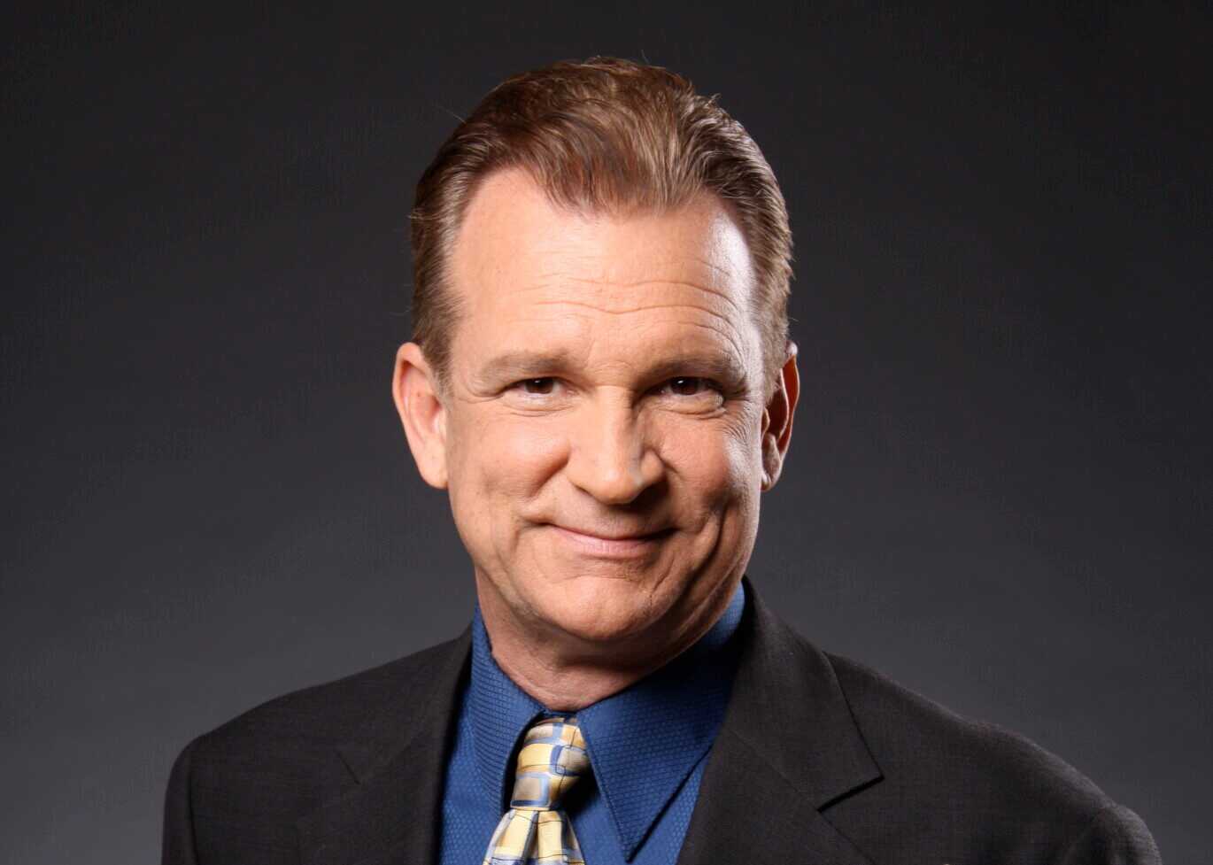 Rick Harris, a musician, holding a trumpet while wearing a suit and tie, posing for a professional portrait.