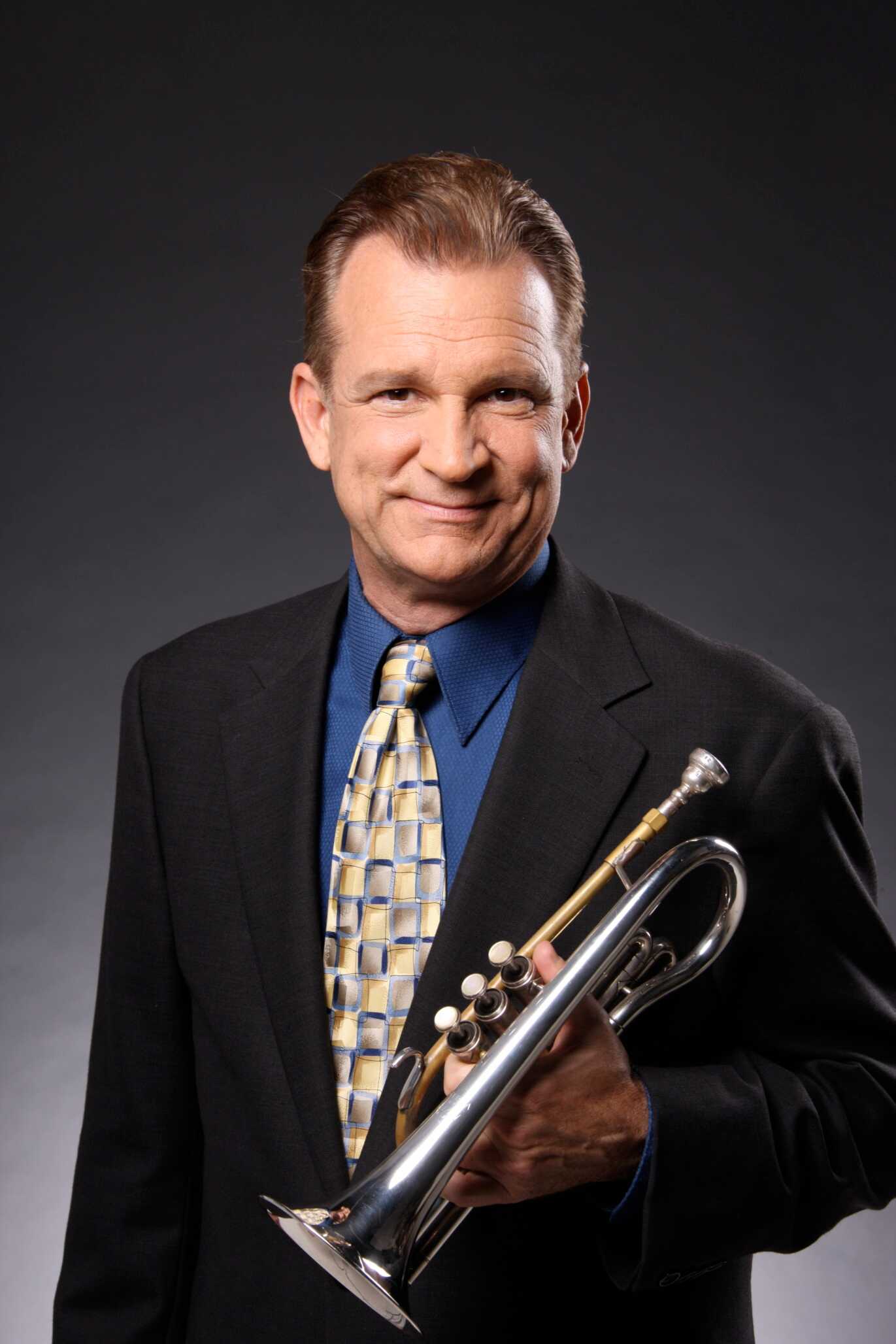 Rick Harris, a musician, holding a trumpet while wearing a suit and tie, posing for a professional portrait.